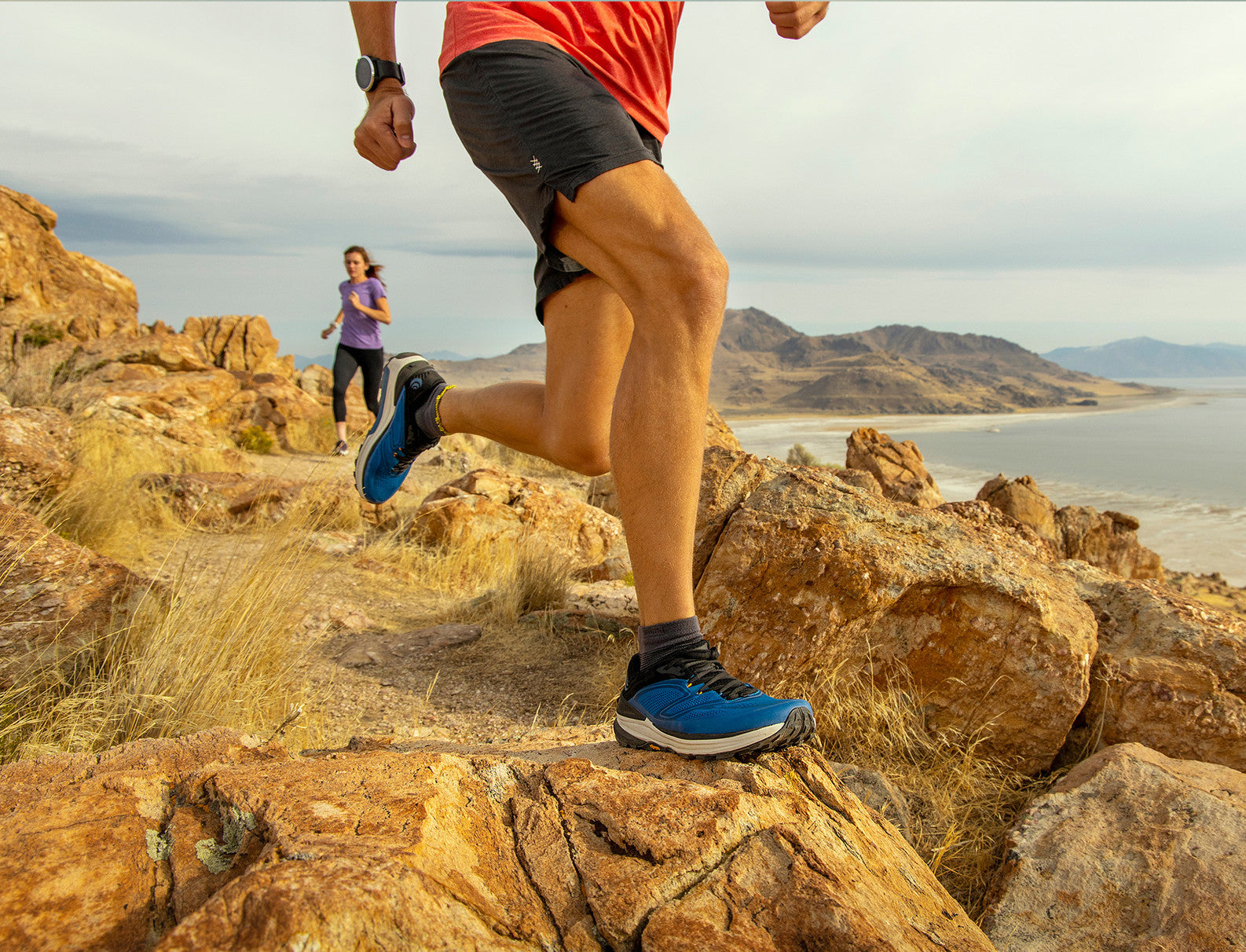 man and woman wearing Topo running shoes while trail running by the ocean